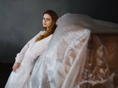 Piyanonun yanında beyaz elbiseli kadın romantizm pozu veriyor.