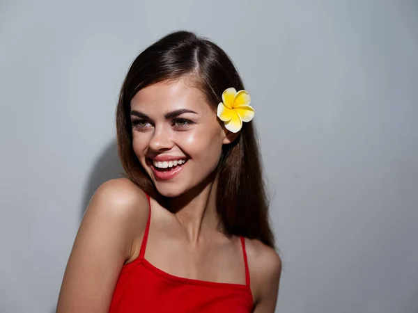 Happy woman with yellow flower in hair and in red t-shirt on gray background cropped view — Stockfoto