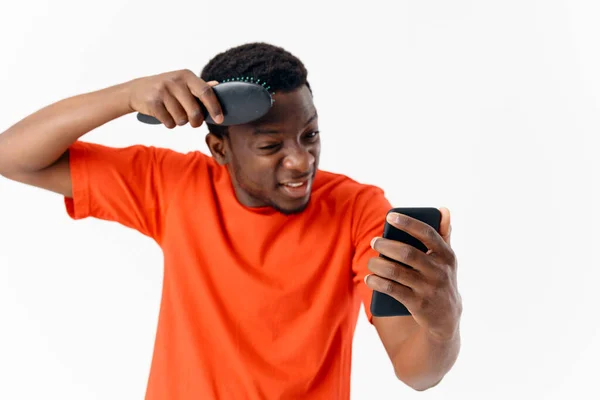 Afro-Amerikaanse kammen zijn hoofd met een telefoon in zijn handen hoofdverzorging — Stockfoto