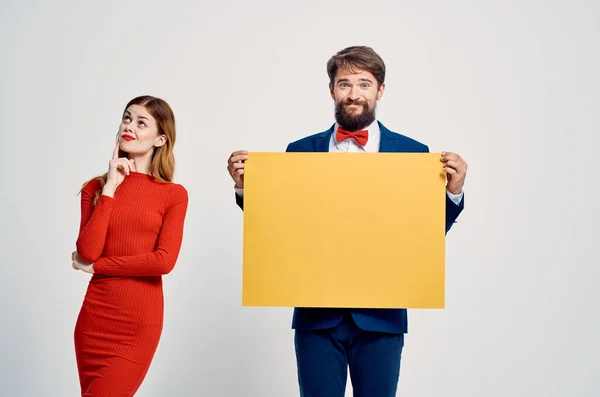 Man en vrouw staan zij aan zij reclame gele mockup poster licht achtergrond — Stockfoto