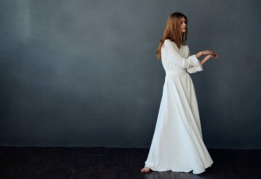 Güzel kızıl saçlı, beyaz elbiseli, eğlenceli dans eden, siyah arka planlı bir kadın.