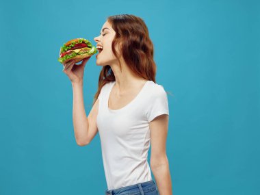 Hamburger yiyen kadın fast food diyeti atıştırmalık mavi arka plan
