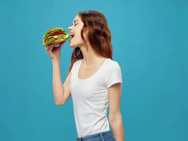 Mujer comer hamburguesa comida rápida dieta bocadillo fondo azul — Foto de Stock
