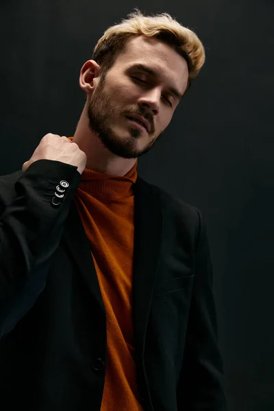 Blond man in a coat and an orange sweater on a dark background — Stockfoto