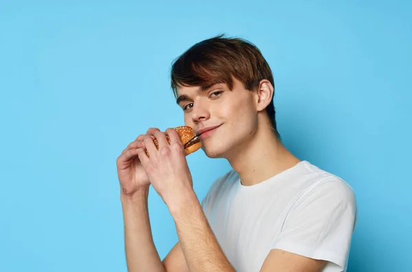 Egy férfi fehér pólóban hamburgert eszik, rágcsálnivalót eszik. — Stock Fotó
