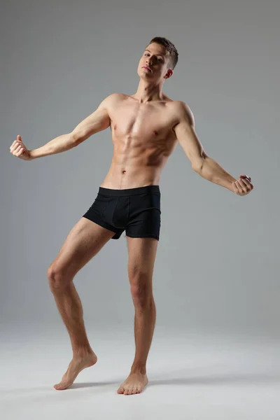Naked man in black panties on a gray background pumped up muscles of the torso barefoot — Stockfoto