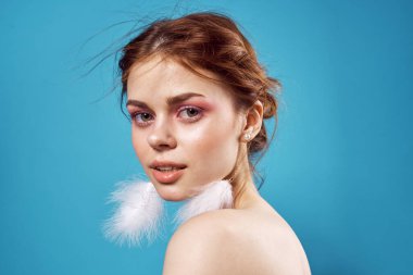 Çıplak omuzlu, parlak makyajlı, tüylü küpeli bir kadın.