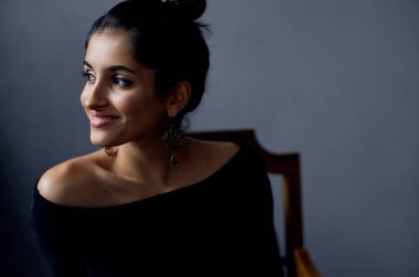 Siyah elbiseli kadın sandalyede oturmuş makyaj yapıyor.