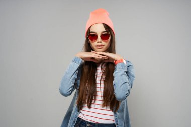 Kot gömlekli güzel kadın güneş gözlüklü pembe şapkalı moda gri arka plan stüdyosu.