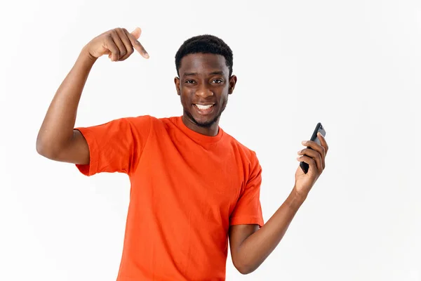 Homem alegre em uma camiseta laranja com um telefone em suas mãos mostra um fundo de luz do dedo — Fotografia de Stock