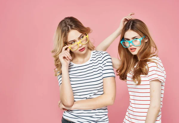 Két barátnő ölelés csíkos pólók sokszínű szemüveg rózsaszín háttér — Stock Fotó