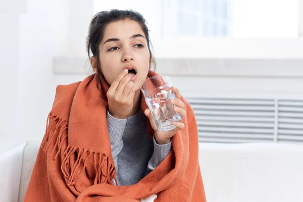 Vrouw bedekt met een deken zit op de bank gezondheidsproblemen koude behandeling — Stockfoto