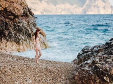 Plajda beyaz mayo giymiş, moda okyanusu pozu veren bir kadın.