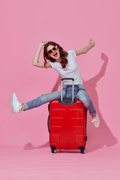 빨간 여행 가방 핑크 색 배경 이 따로 있는 선글라스를 낀 쾌활 한 여성 — 스톡 사진