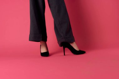 Pembe arka plan pozu veren siyah ayakkabılı kadın bacakları.