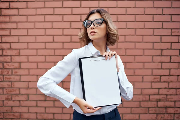 Veselá žena manažer v bílé košili dokumenty v ruce cihlové pozadí — Stock fotografie