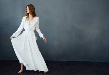 Beyaz elbiseli güzel bir kadın karanlık arka planda dans ediyor.