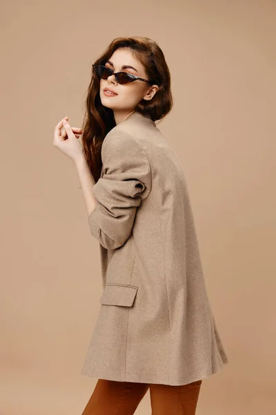 Mulher na moda em casaco e óculos no fundo bege vista lateral — Fotografia de Stock