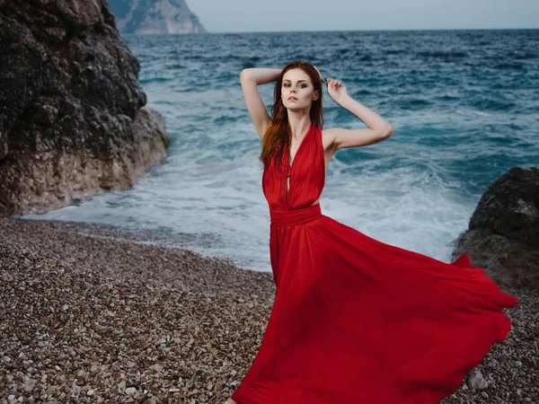 Όμορφη γυναίκα με κόκκινο φόρεμα ποζάρουν κοντά στο βράχο παραλία ρομαντική σχέση διακοπές — Φωτογραφία Αρχείου