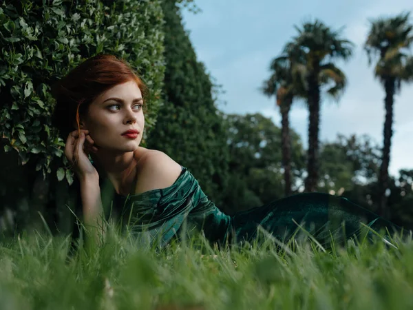 Όμορφη γυναίκα με πράσινο φόρεμα βρίσκεται στο γρασίδι στον κήπο της φαντασίας — Φωτογραφία Αρχείου