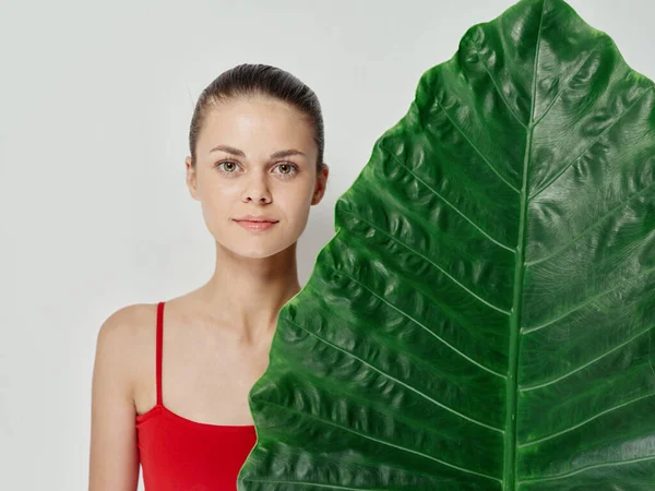 Bonita mujer con hoja de palma rojo traje de baño fondo claro —  Fotos de Stock