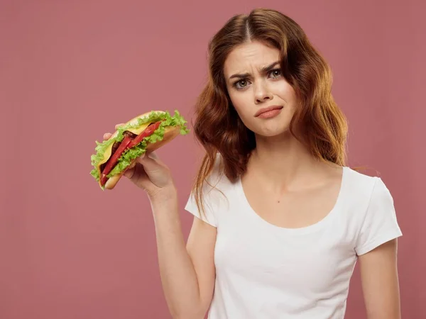 Donna in bianco t-shirt hamburger fast food rosa sfondo — Foto Stock