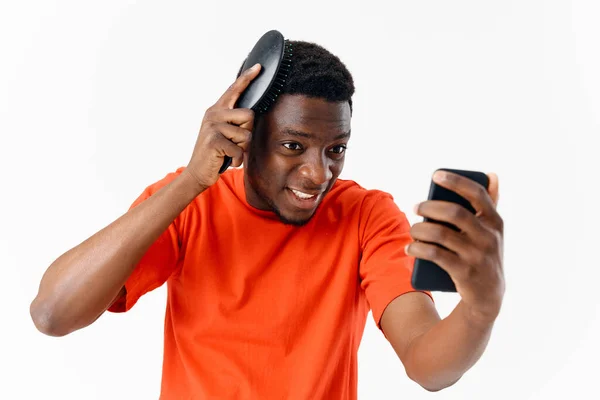 Um homem de aparência africana penteando a cabeça com um telefone em suas mãos — Fotografia de Stock