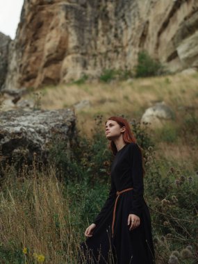 Siyah elbiseli, kızıl saçlı kadın doğa yolculuğu yapıyor.