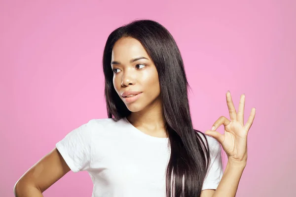 Vrolijke vrouw van afrikaanse verschijning in wit t-shirt lang haar roze achtergrond — Stockfoto