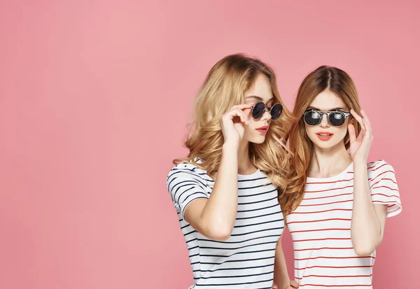 Két barátnő áll egymás mellett csíkos pólók szemüveg divat nyár rózsaszín háttér — Stock Fotó