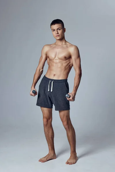 Sportos férfi rövidnadrágban, súlyzókkal a kezében, felpumpált testhossz motivációval. — Stock Fotó