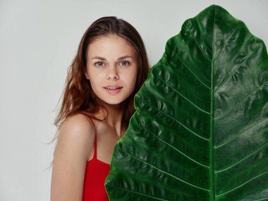 Palmiye yaprağının yanındaki kırmızı tişörtlü mutlu kadın. 