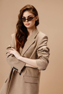 Paltolu ve gözlüklü romantik kadın bej arka planda ileriye bakıyor.