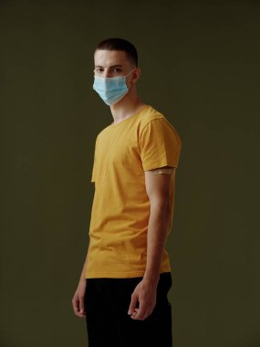 Sarı tişörtlü ve tıbbi maskeli bir adam.