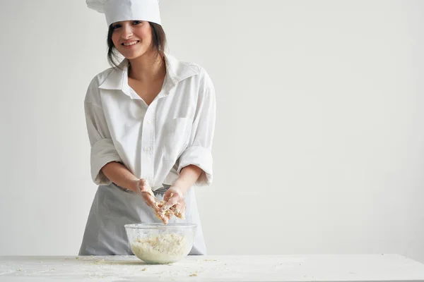 cheerful woman baker in chefs uniform rolls the dough on the table work