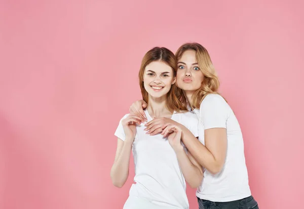 Két nő áll egymás mellett fehér pólóban barátság érzelmek rózsaszín háttér — Stock Fotó