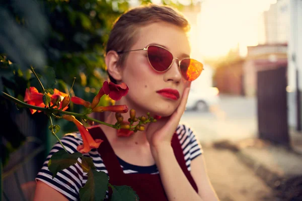 Kvinna i solglasögon står bredvid en buske med blommor i gatan livsstil — Stockfoto