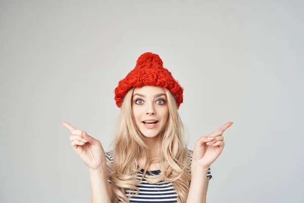 Bonita rubia en un sombrero rojo gesticulando con sus manos fondo de luz de moda —  Fotos de Stock