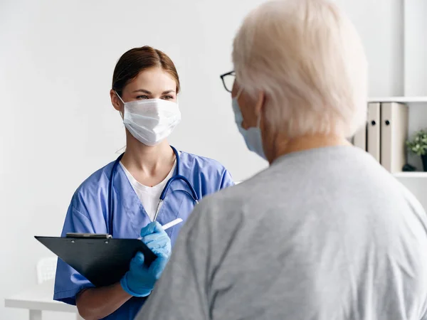 Una anciana con una máscara médica mira una composición de enfermera en masa y con documentos en un pasaporte covid hospital — Foto de Stock