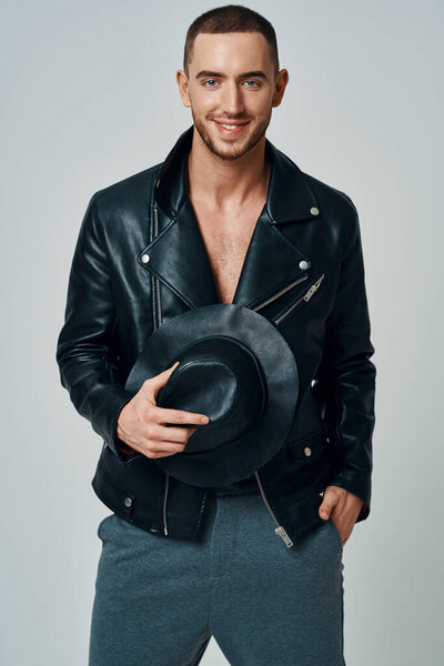 man in black leather jacket hat posing fashion confident light background