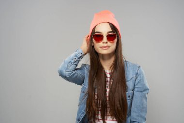 Kot gömlekli güzel kadın güneş gözlüklü pembe şapkalı moda gri arka plan stüdyosu.