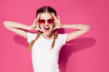 Beyaz tişörtlü, atkuyruklu duygusal kadın. Moda kıyafetler. Pembe arka plan.