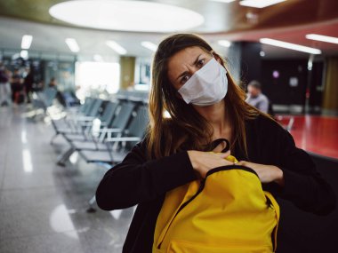 Tıbbi maske takan kadın yüz ifadesinden memnun değil sarı sırt çantası havaalanı