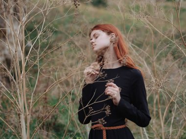 Kızıl saçlı kadın siyah elbise dağlarda özgürce yürüyor.