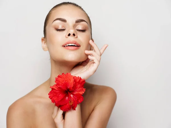 Beautiful woman with bare shoulders closed eyes light background red flower — Stock Photo, Image