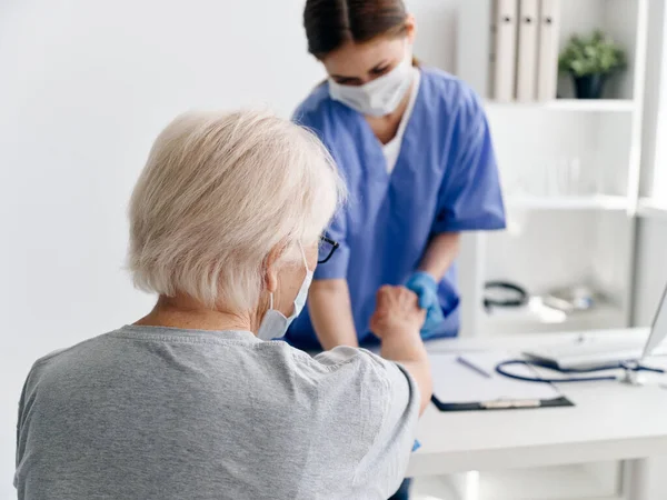 Verpleegster aan tafel in het kantoor en vrouw gepensioneerde injectie infectie coronavirus covid paspoort — Stockfoto