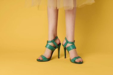 Kadın bacaklarında yeşil ayakkabılar yakın plan sarı arka plan pozu veriyor.