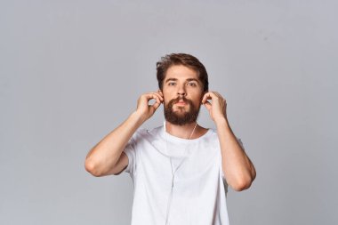 Beyaz tişörtlü neşeli sakallı adam elini yüzüne yakın tutuyor.