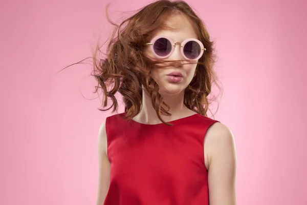 Roztomilý červenovlasá dívka nosí sluneční brýle módní růžové pozadí — Stock fotografie