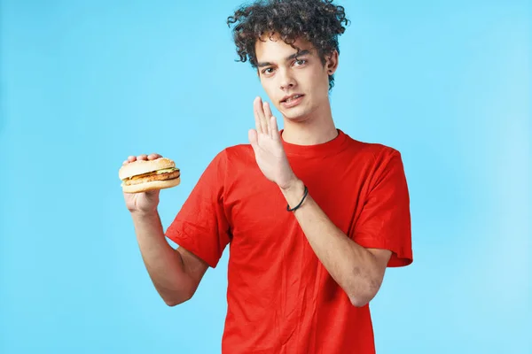 Τύπος με σγουρά μαλλιά σε κόκκινο t-shirt χάμπουργκερ fast food μπλε φόντο — Φωτογραφία Αρχείου